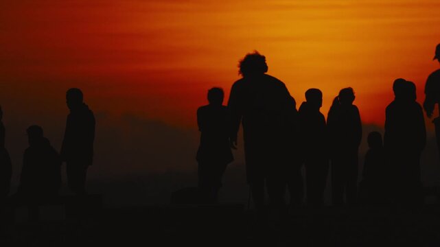 Silhouetted figures of diverse individuals walking and gathering against a vibrant sunset sky, showcasing the dynamic movement and interaction in an outdoor setting