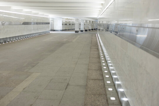Empty modern pedestrian underpass with marble walls and bright line lighting