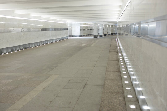 Empty modern pedestrian underpass with marble walls and bright line lighting