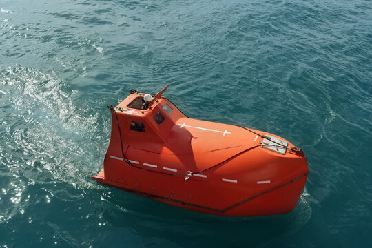 orange freefall lifeboat floating on calm blue sea with crew member inside, showcasing maritime safety equipment and emergency evacuation capability on board a commercial vessel