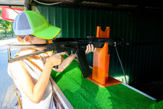boy in a bright green cap aims from a black automatic rifle on a stand in an outdoor shooting range