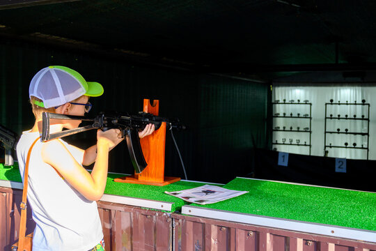 boy aims from an automatic rifle at black metal targets in the shooting gallery of an amusement park