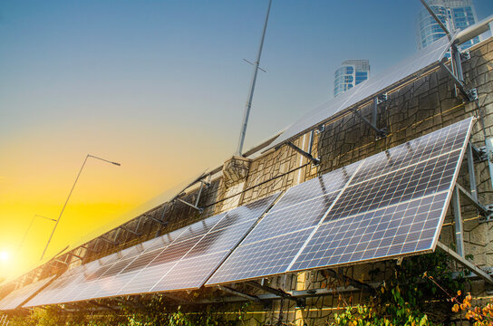 Solar panals under a vibrant sunset sky, reflecting golden hour on city wall. Alternative energy for future of environment.