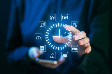 Fototapeta premium Hands interacting with digital time management icons while holding a smartphone in a modern setting during the evening