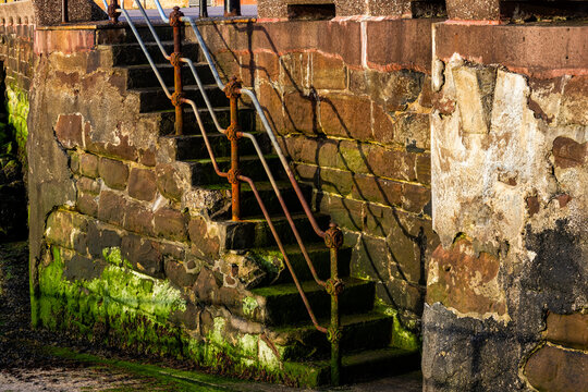 Rusted railings cast shadows down old stone steps covered in algae at low tide