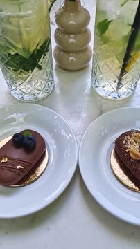 Two elegant chocolate popsicle cakes sit on the table near tall glasses of refreshing mint mojito lemonade with ice. The dessert is topped with peanuts, blueberries and gold foil
