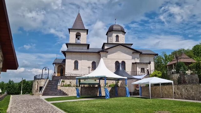 Outdoor view of Varzaresti Monastery with a cobblestone courtyard and a prominent bell tower with a dark dome topped with Christian crosses under a beautiful sky
