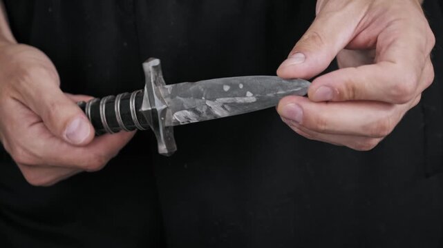Close-up of a person carefully examining the sharp edge and ornate hilt of a classic steel dagger. This historical weapon represents danger craftsmanship and medieval combat.
