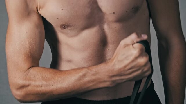 Close-up on a shirtless athletic mans torso performing a chest fly exercise with a black resistance band. The movement highlights pectoral and arm muscle definition.