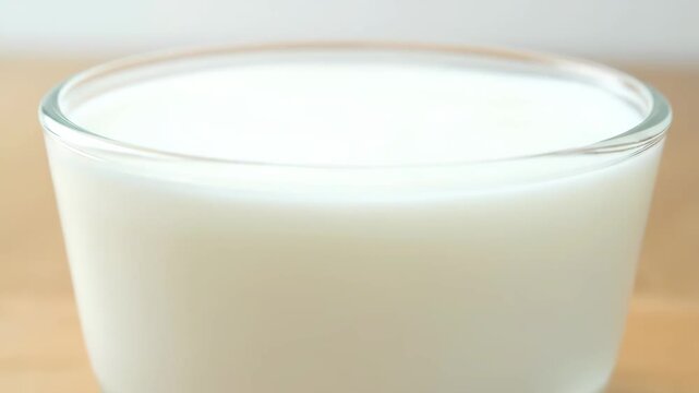 Close-up high angle shot of fresh white milk poured into a clear glass tumbler, highlighting healthy dairy beverage and breakfast drinks.