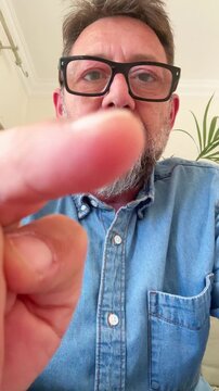 Middle-aged bearded man wearing glasses and a denim shirt using his finger to scroll, swipe, and tap on a futuristic transparent screen, interacting with a user interface