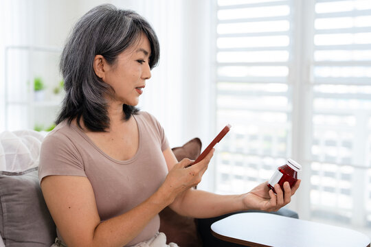 Asian woman holding bottle of food supplement or medicine using computer typing searching online prescription  pill bottle  information online.