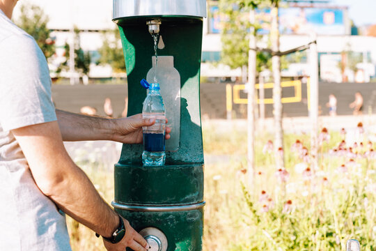 Eco-minded man refilling reusable plastic bottle at outdoor water fountain