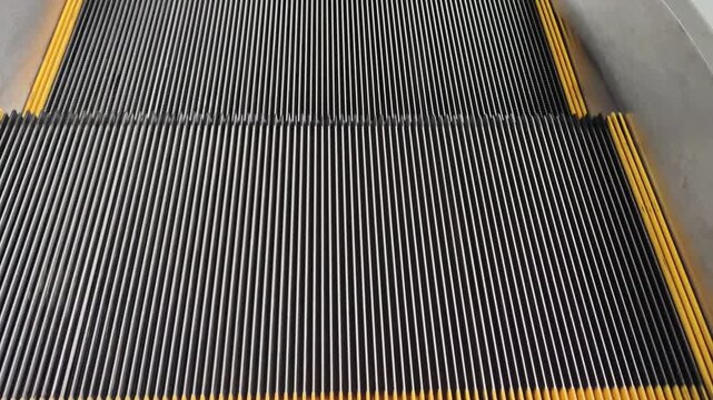 Grooved metal escalator steps move continuously in a close up view. Silver stairs feature yellow safety borders. Concept illustrates urban transportation and mechanical engineering motion.