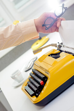 Author holding glasses while typing on vintage typewriter