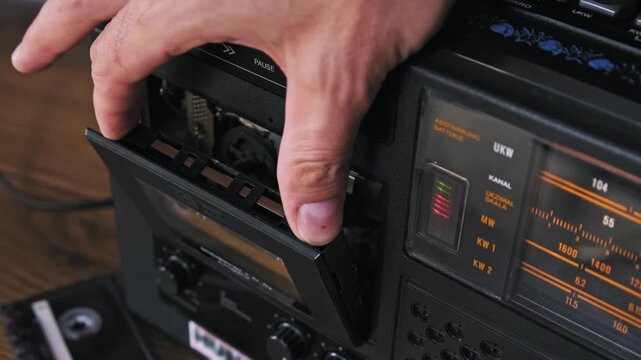 Close-up of a hand pressing the stop eject button on a vintage stereo to remove a yellow audio cassette. The mechanical action of the deck door highlights the tactile user interface of