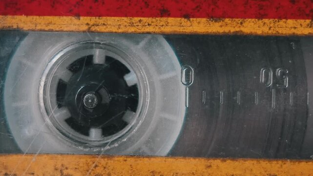 Extreme close-up macro of a single spinning reel on a grungy audio cassette with scratched plastic. The worn texture and numeric counter marks inside the vintage player highlight analog age.