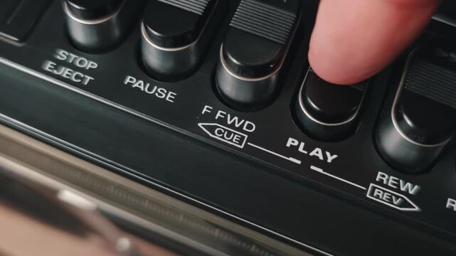 Extreme macro shot of a finger pressing the play button on a vintage cassette player. The textured black key and white labels highlight the retro audio panel.