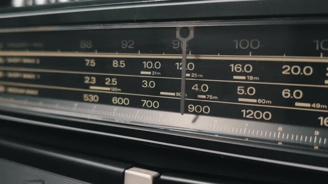 Close-up shot of tuning a radio dial on a retro black boombox. The indicator scanning the analog frequency scale highlights the classic 1980s portable stereo system.