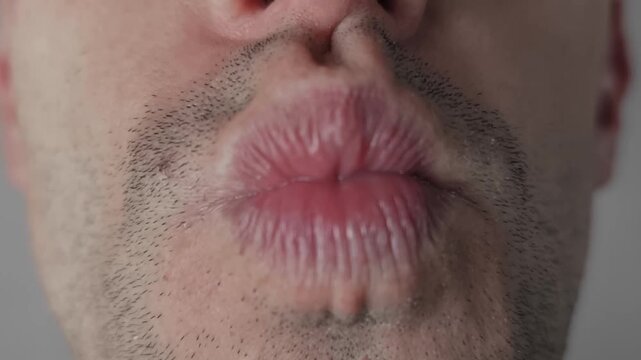 Close-up focuses on an unshaven male mouth puckering for a kiss before relaxing into a smirk. The macro shot details stubble and lip texture in a playful romantic gesture.