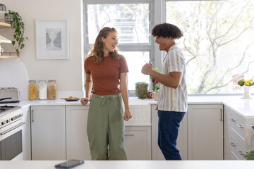 Obraz premium Couple smiling and talking while standing in home kitchen in casual clothes near jars with phone