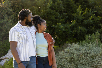Fototapeta premium African American couple posing together in sunlit park wearing jeans, bracelet and hoop earrings
