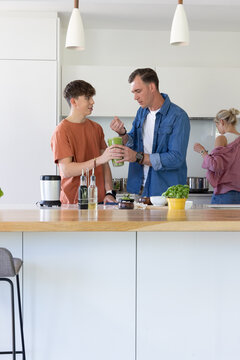 Family with parents and teenage son preparing food and sharing green bottle at kitchen island