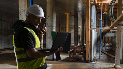 Fototapeta premium Building renovation, site supervisor uses laptop and radio inside unfinished structure, coordinating construction safety and installation work