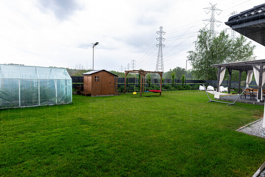 Rain falling on green garden lawn with backyard structures