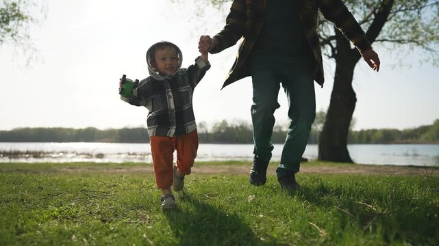 Family running together in park. Child happily running outdoors, holding hands with father. Family nature. Outdoor park run with family. Father, child enjoy run in park. Happy family outdoor playtime