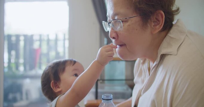 A caring toddler provides nutritional support to an elderly grandmother, highlighting a tender moment of home care and intergenerational family bonding.