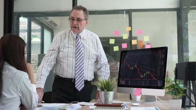 An experienced manager discussing financial stock market data with a colleague in a professional office