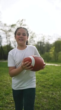 Smiling child holding rugby football. Child enjoys playing tball on grass in park. Active kid with football outdoors. Happy child playing rugby football, running on green grass. Football fun