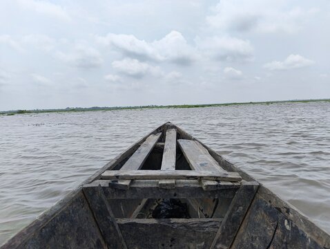 A weathered wooden boat floats on a large body of water under a cloudy sky