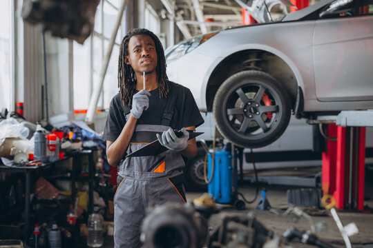 African American auto mechanic thinking in garage, holding clipboard and pen, planning car maintenance