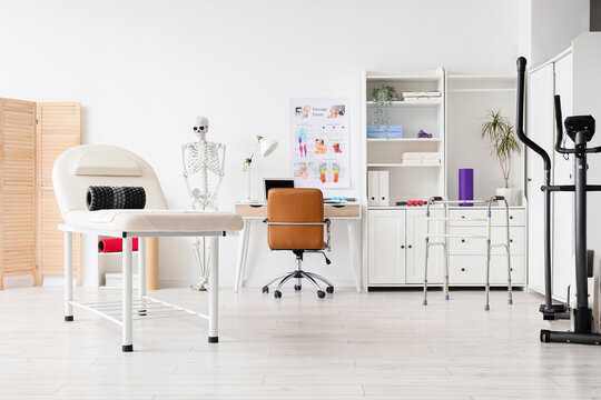 Modern physical therapy and rehabilitation clinic interior with medical equipment and anatomical skeleton model, the room includes a massage table with a foam roller