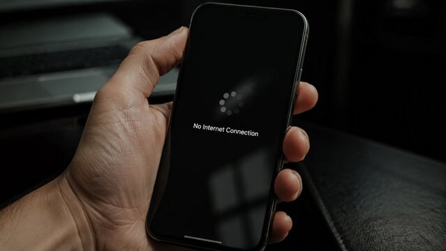 Hand holding smartphone showing no internet connection status and a loading spinner. Represents connectivity downtime and user waiting for data restoration