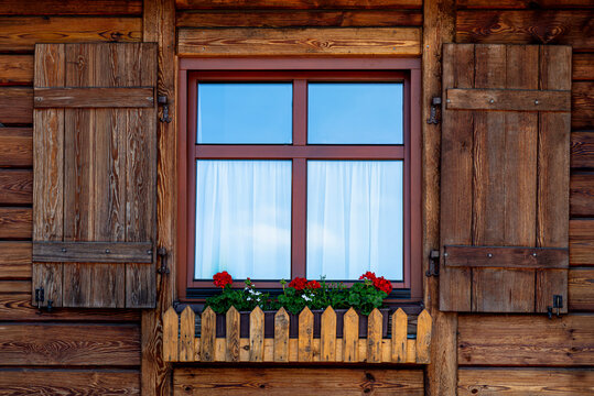 Wooden house window with rustic shutters and blooming red flowers