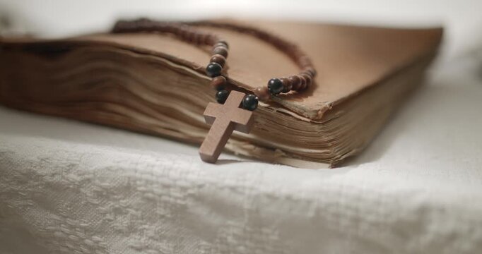 Religion, holy bible and rosary on white cloth on a table for prayer. Christian, faith and spiritual book with wooden rosary beads and cross for reading, worship or praying to God for compassion. Reli