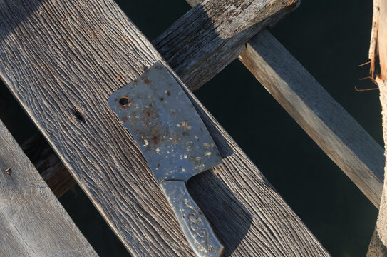 an old, rusted metal meat cleaver knife resting on the weathered grey timber boards of a rustic maritime platform