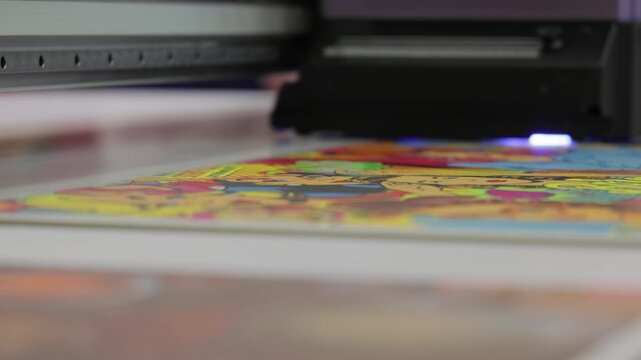 Industrial uv printer head moving over colorful printed sheet in manufacturing facility.