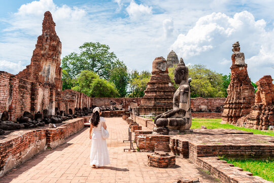 Young female tourist in a white dress walking through the ancient brick ruins of Wat Mahathat in Ayutthaya Historical Park, Thailand