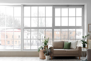 Obraz premium Interior of light living room with green houseplants, sofa and window