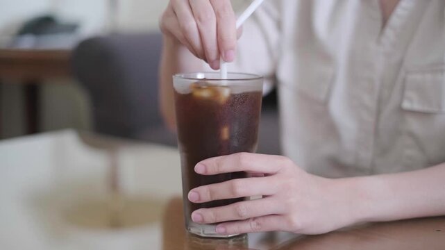 Close-up hand stirring coffee in a cup glass on table, morning caffeine lifestyle concept