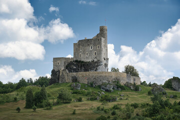Fototapeta premium Mirow Castle in Poland on a limestone hill with green landscape and cloudy summer sky, a historic travel landmark in rural scenery