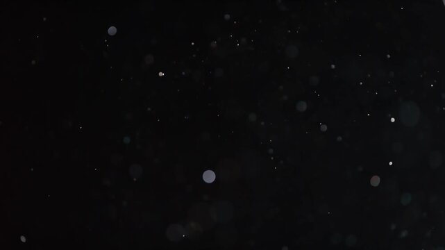 Abstract motion of shimmering particles floating and swirling against a dark background, creating a dynamic and enchanting visual effect.