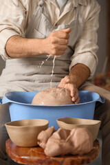 Fototapeta premium Potters hands squeezing water from clay in blue basin, pottery crafting process, ceramic art workshop