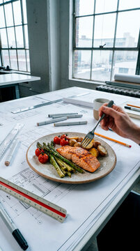 Healthy grilled salmon and asparagus plate at architect drafting desk