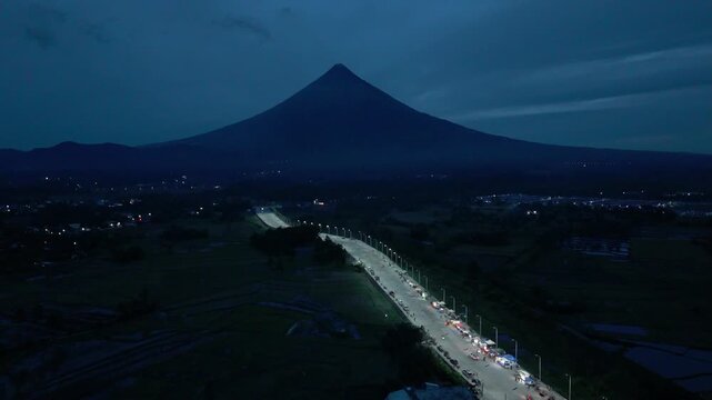 Aerial drone captures Mayon Vocano in the distance and the Bypass Road lights in Albay, Philippines. Ideal for documentaries and tourism content.