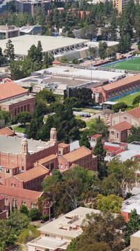 Aerial shot flying over University of California Los Angeles campus with red brick buildings and sports fields on clear summer day in suburban neighborhood